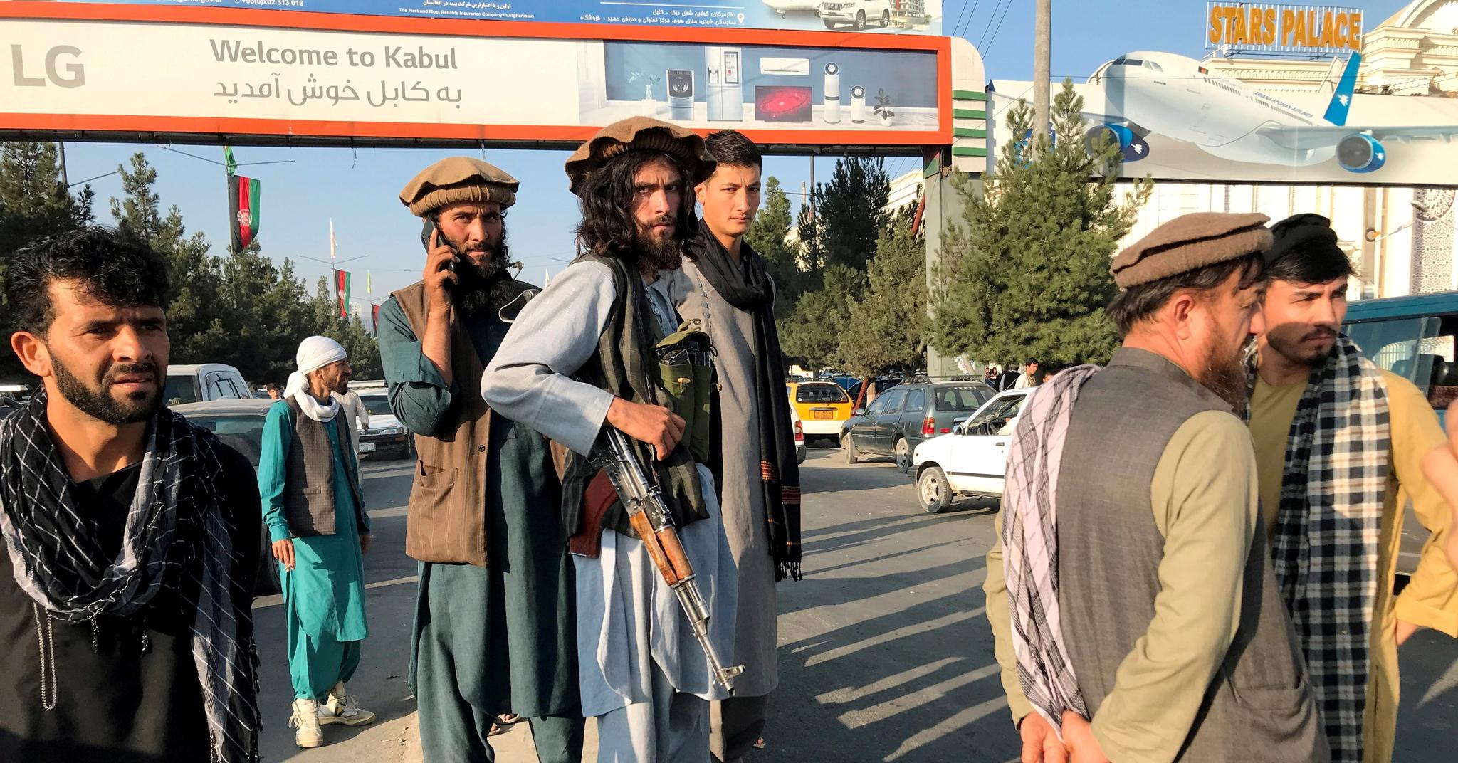 Her står medlemmer av Taliban utenfor Hamid Karzai internasjonale lufthavn i Kabul, hvor det pågår en kaotisk evakuering.
