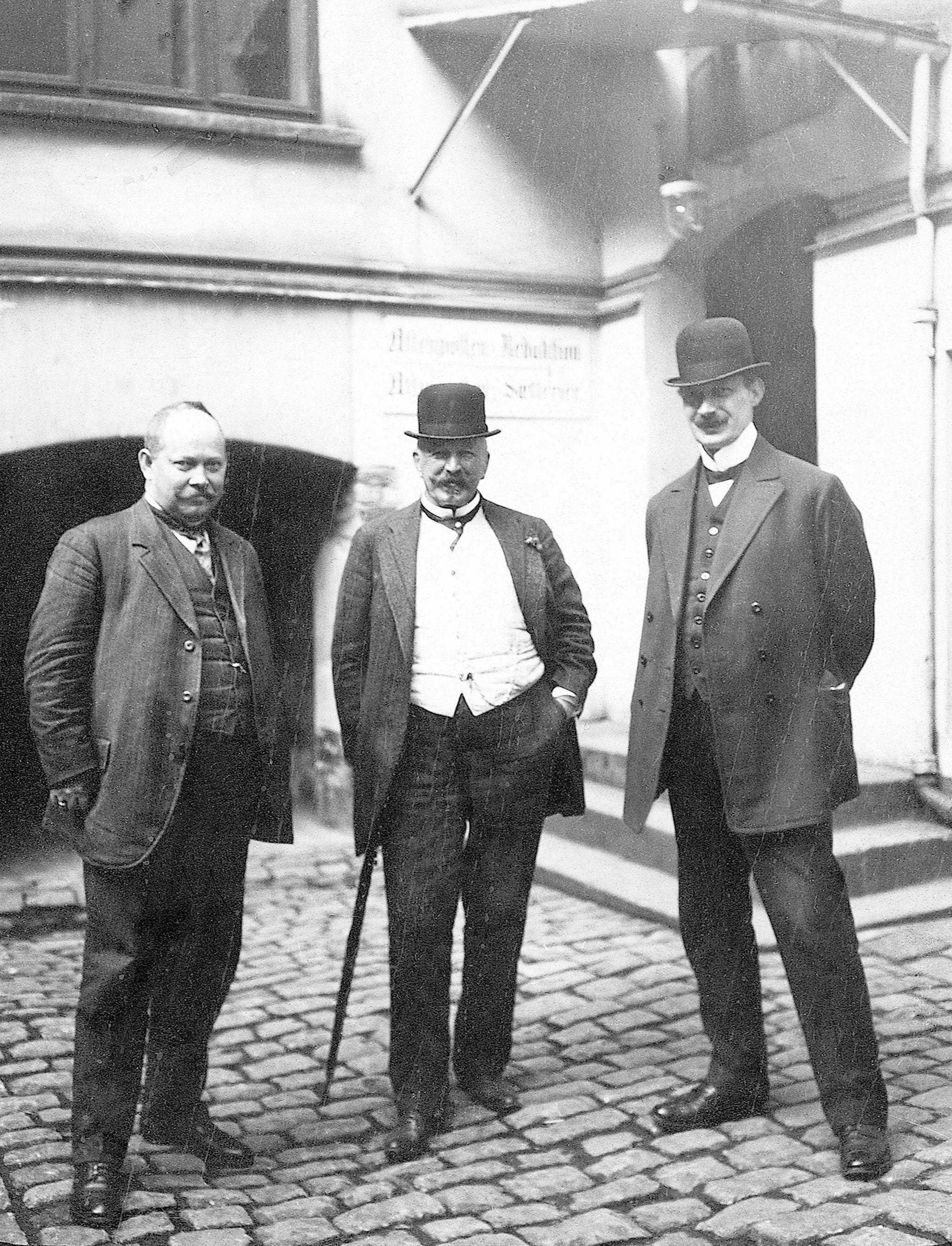 Amandus Schibsted (i midten) med spaserstokken. Bildet er tatt med Aftenpostens første kamera på den gamle gårdsplassen i Akersgata i 1912.