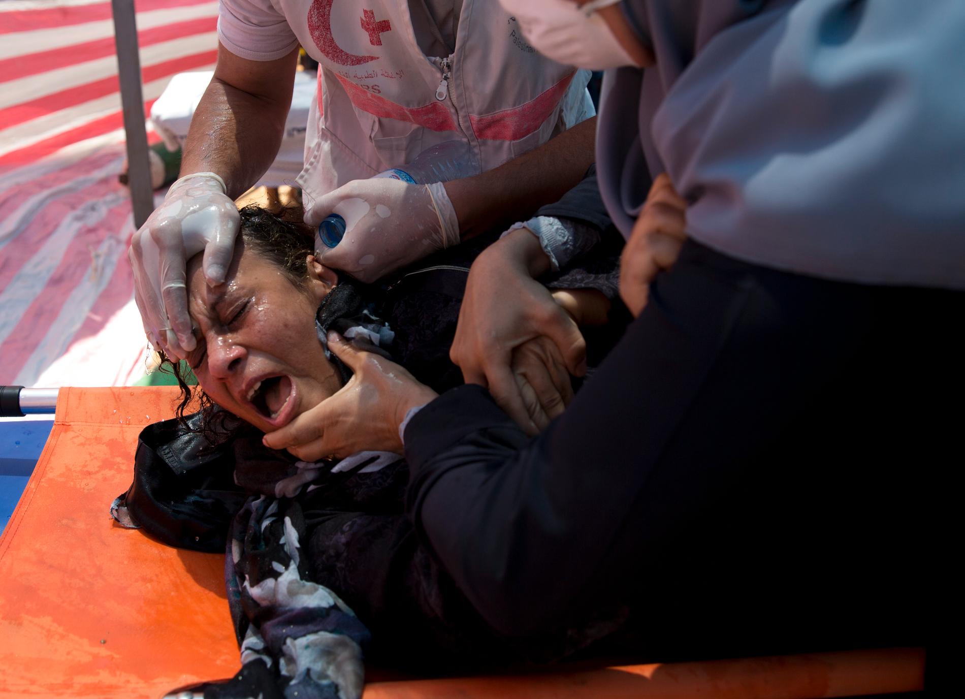 TÅREGASS: Helsearbeidere behandler en palestinsk kvinne som ble rammet av israelsk tåregass under mandagens demonstrasjon på Gazastripen.