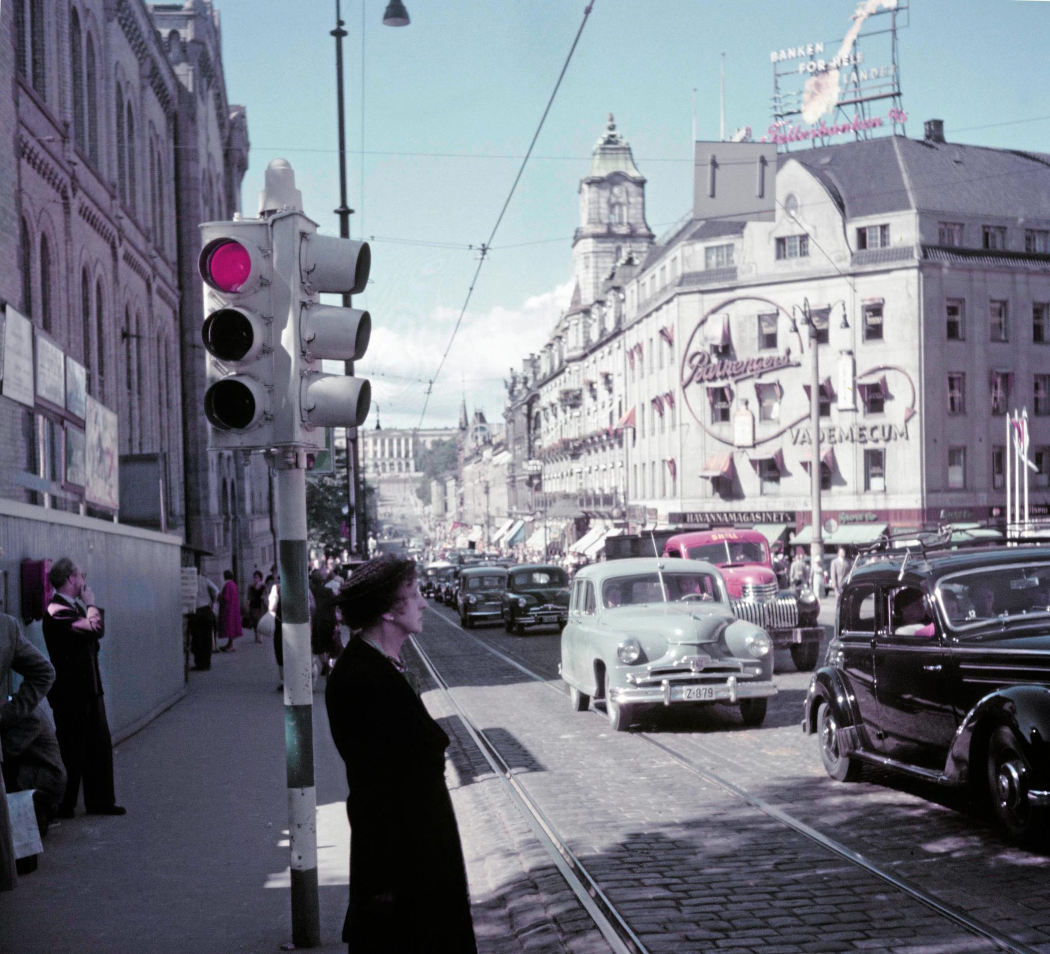 Oslo 1950 ( ca ) Karl Johans gate med mennesker, biler. Trikkeskinner. Reklameskilt på Grand Hotel gården: Fellesbanken, Vademecum fra Barnengen.