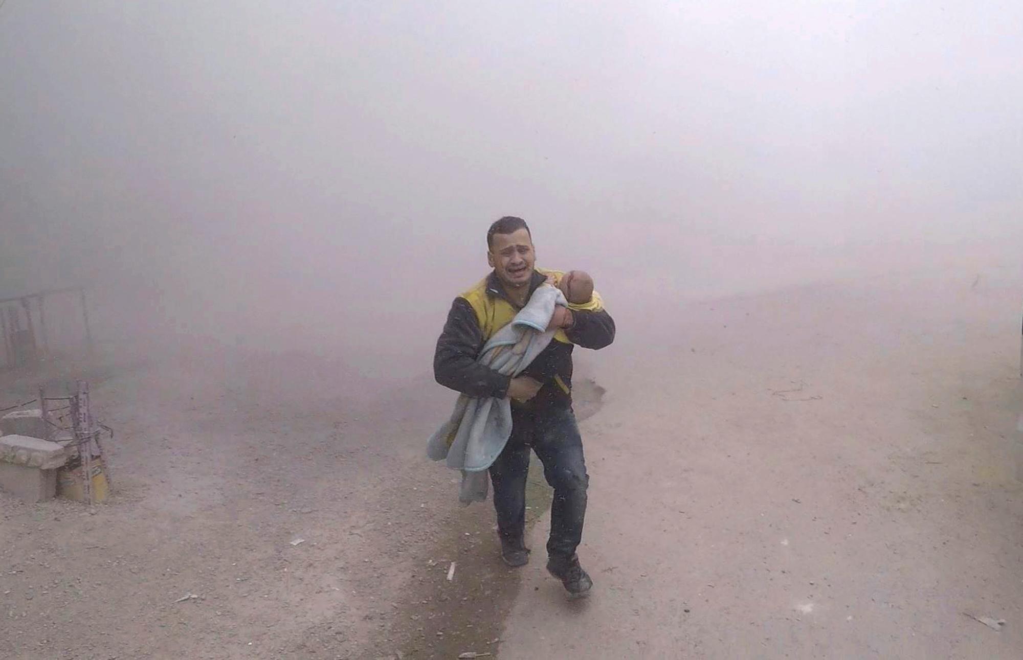 Dette bildet fra Hvite hjelmer viser ifølge gruppa en frivillig som bærer sin sårede sønn etter et bombeangrep i utkanten av Damaskus tirsdag. Foto: Syrian Civil Defense White Helmets via AP / NTB scanpix