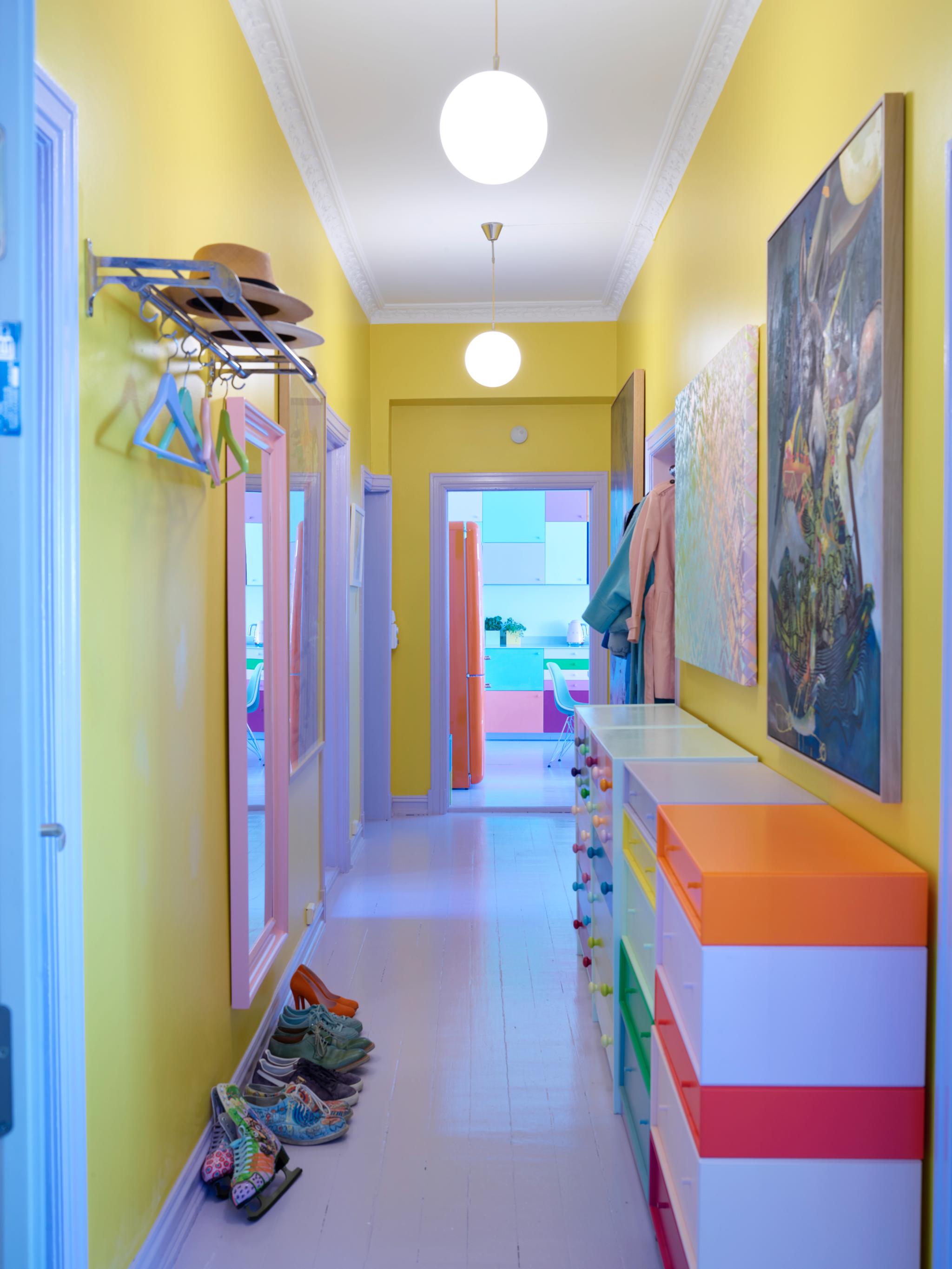Du kan ikke unngå å bli i godt humør når du åpner døren og møtes av denne lysende gule gangen. Ulike kommoder med mangefargede skuffer og et stort rosa speil gjør inntrykket komplett.