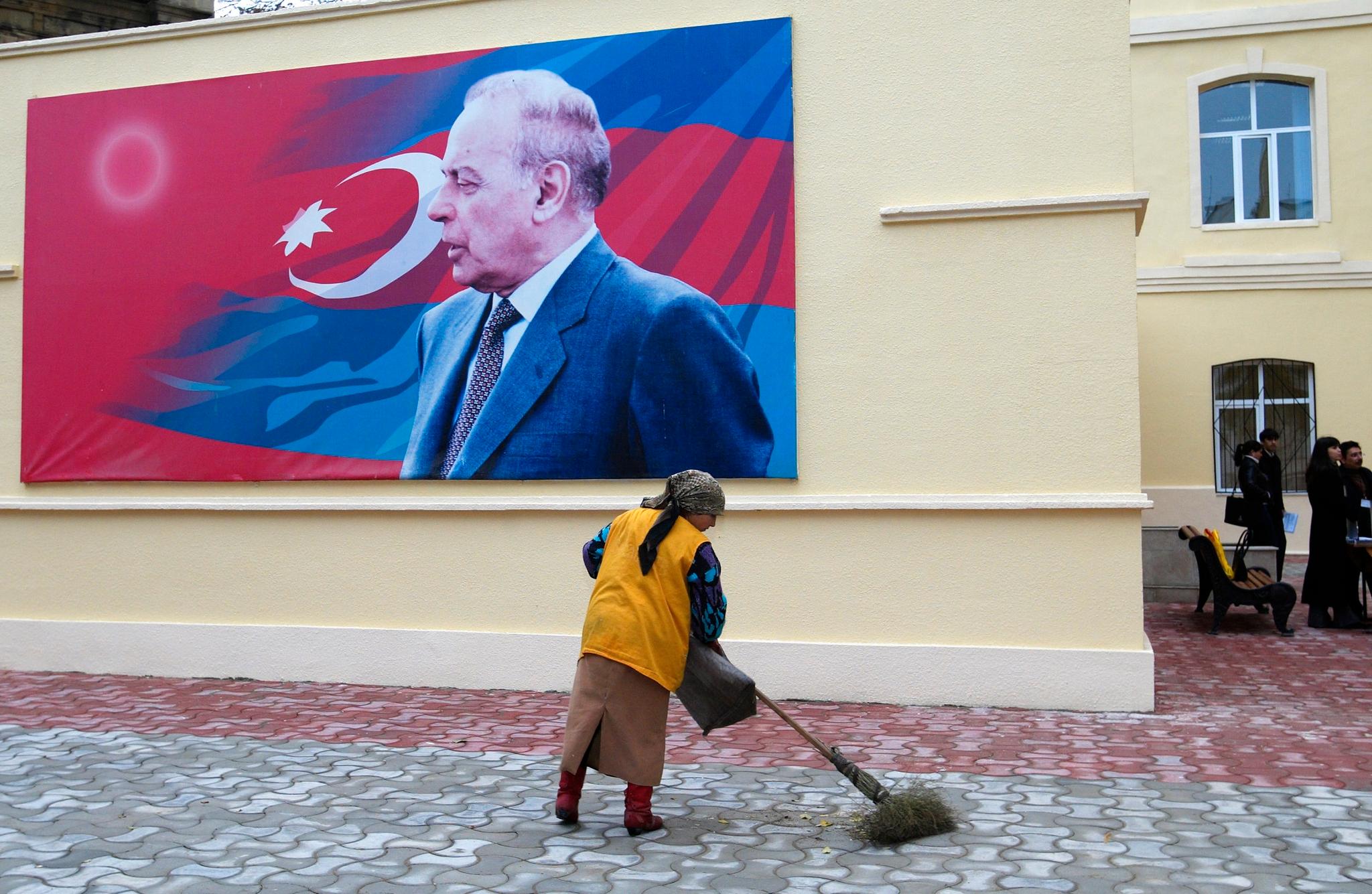 En dame koster gaten foran et bilde av avdøde president Hejdar Alijev. Alijev-dynastiet har styrt Aserbajdsjan med hard hånd siden 1993. Sønnen Ilham Alijev arvet makten i 2003.