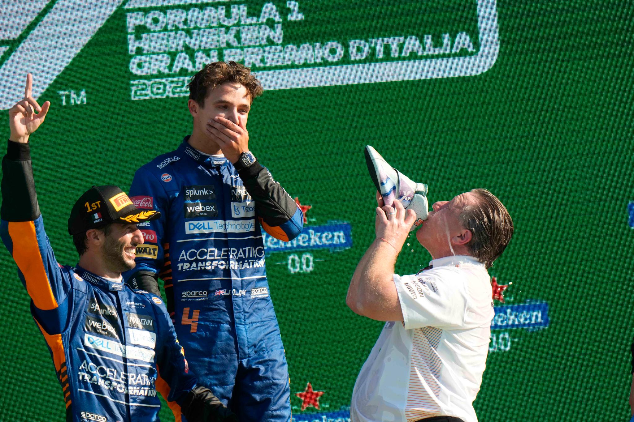 Daniel Ricciardo (t.v.) og Lando Norris (midten) deler en «shoey» med McLaren direktøri McLaren Zak Brown (t.h.).