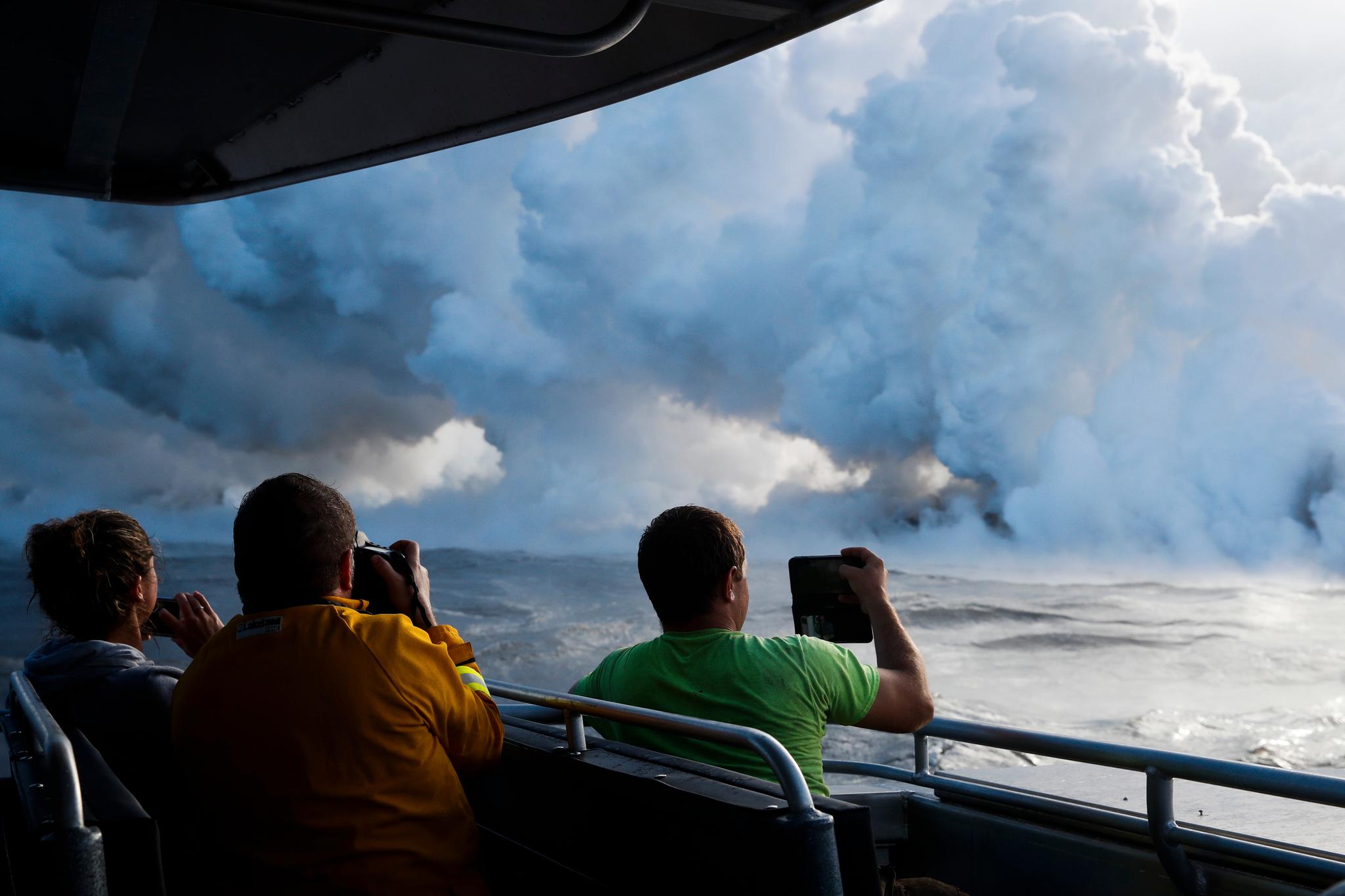 Turister på en passerende båt tar bilder av dampsøylene som oppstår der lavaen møter havet.